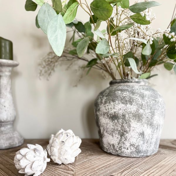 Aged stone vase decor with greenery and whitewashed artichokes, farmhouse style.